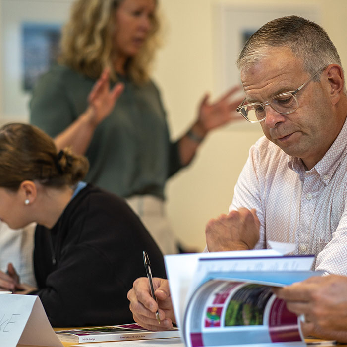 Man med sin lärobok i förgrunden och en (suddig) kvinnlig instruktör i bakgrunden.